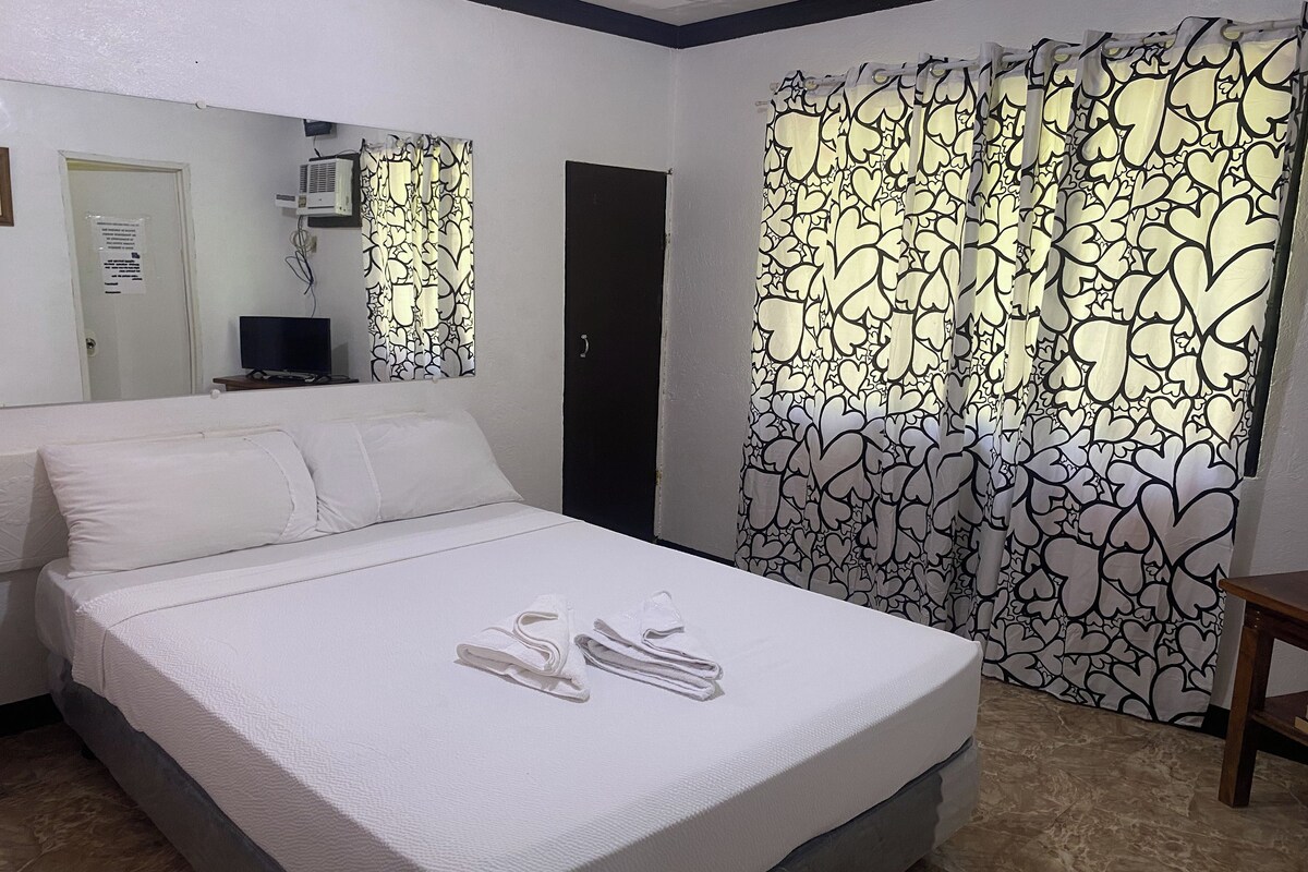 A hotel room with a bed, a flat-screen TV, a mirror, and a door.