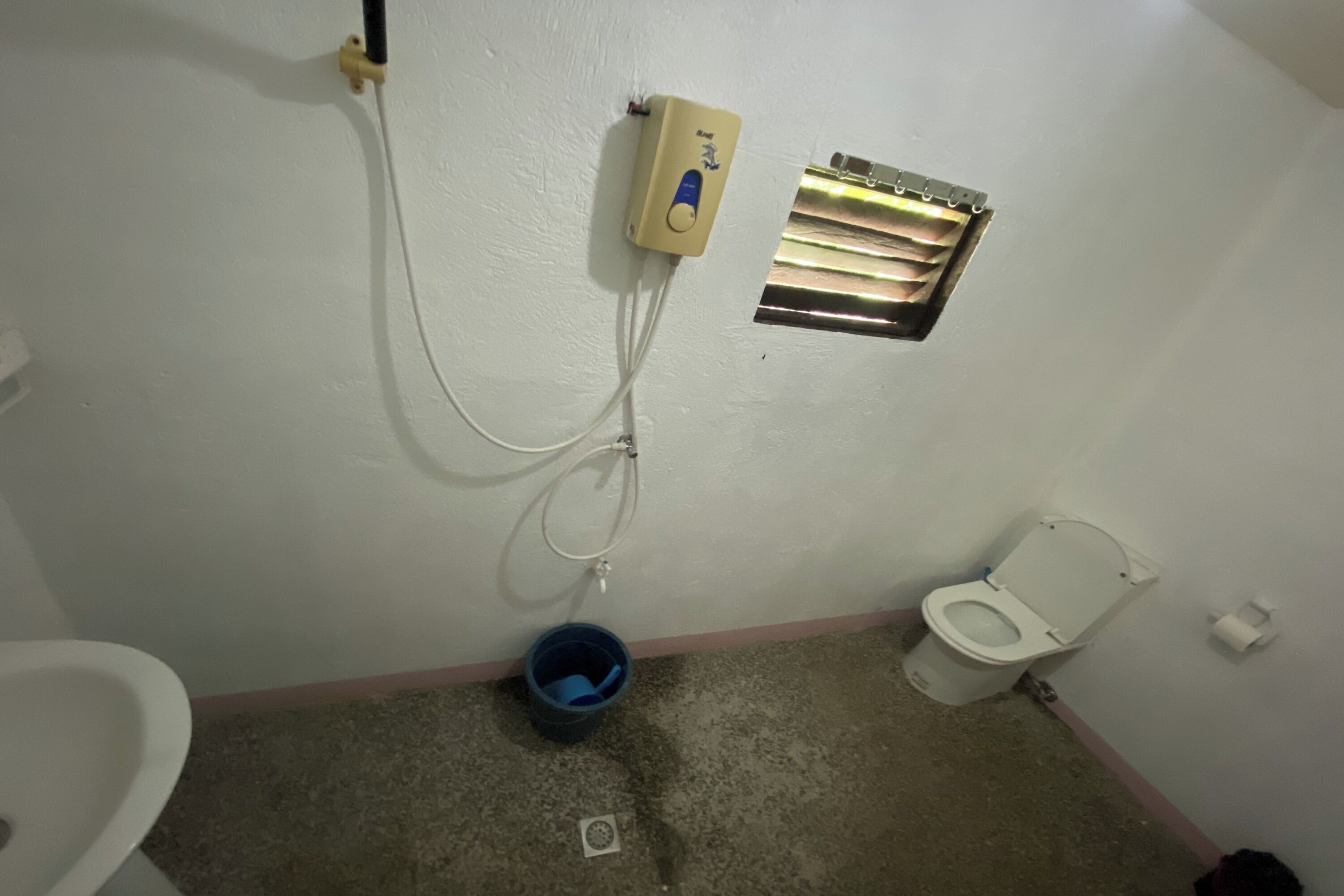 Un baño con inodoro, bidé, un cubo azul y calentador de agua en la pared.