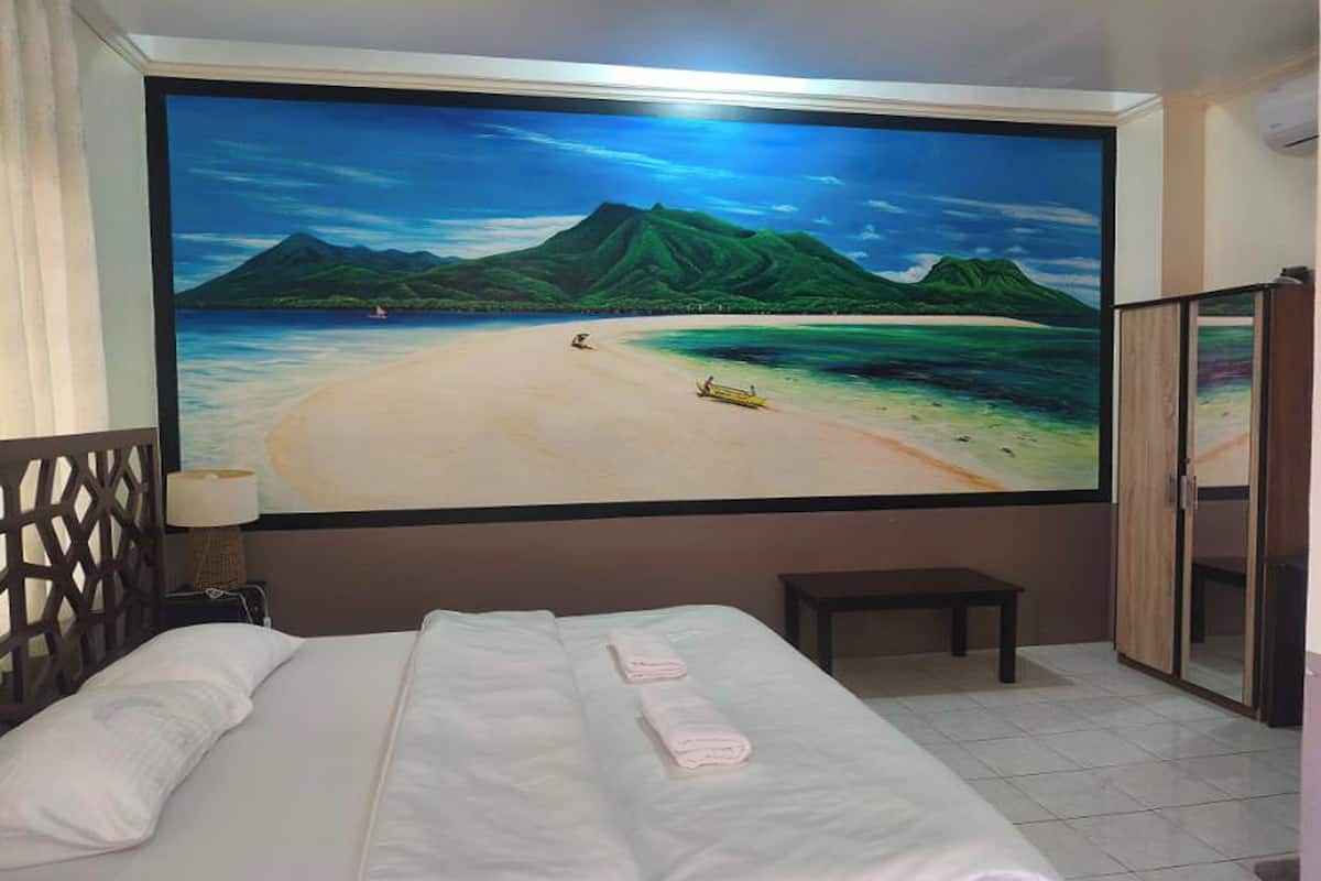 A hotel room with a large beach mural on the wall, a bed with white linens, a wooden headboard, a small bench, and a wardrobe.
