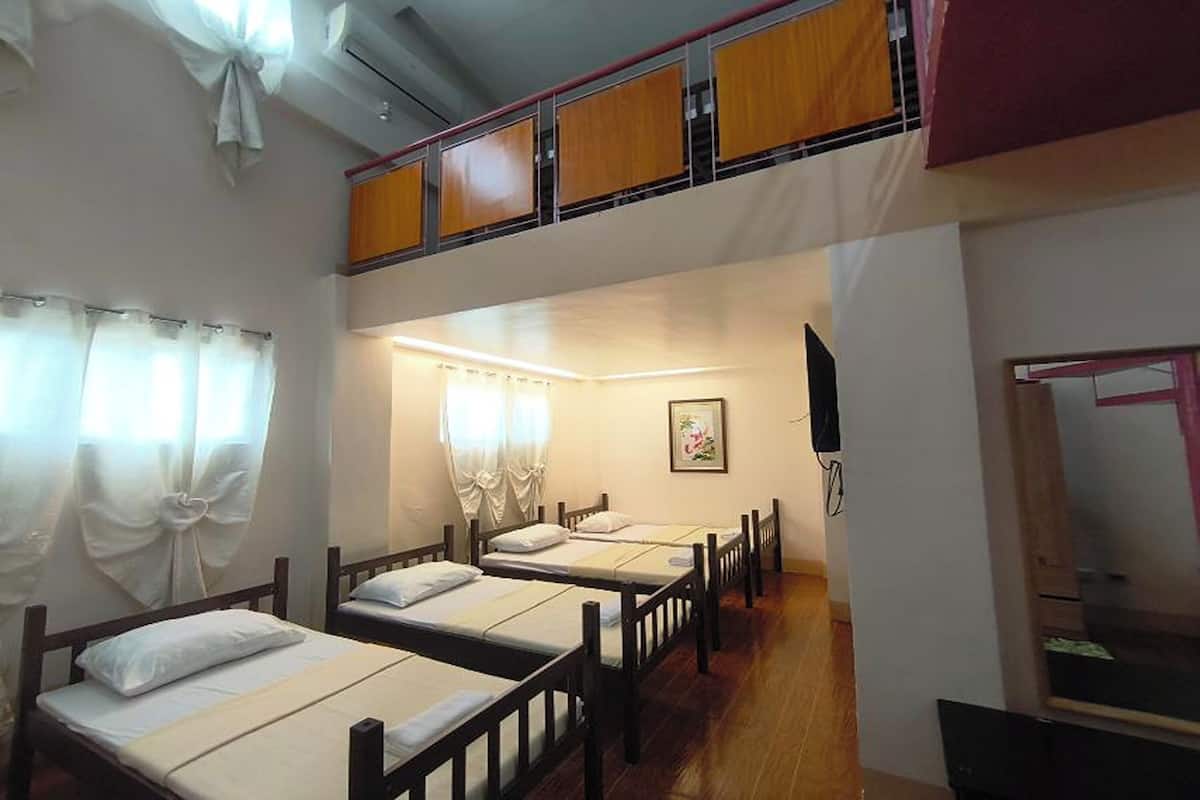 A dormitory room with bunk beds, a small TV, and a window with curtains.