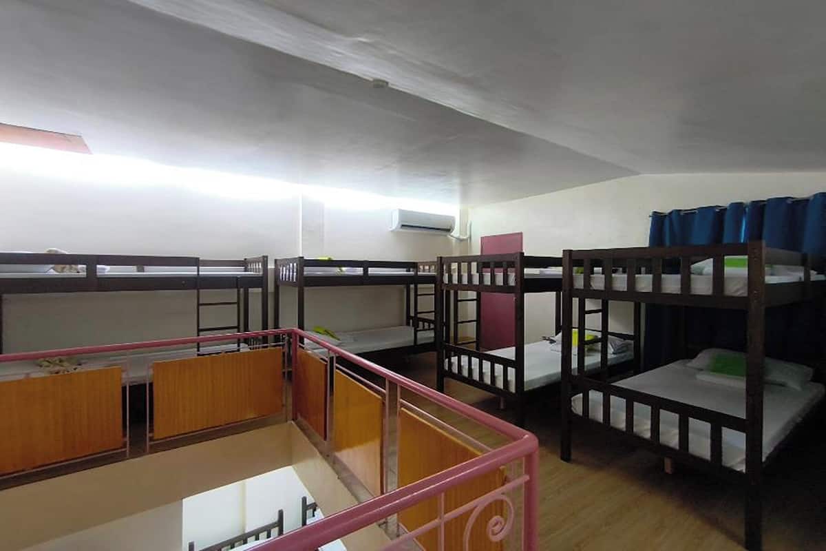 A dormitory room with bunk beds, a wooden desk, and a pink railing.