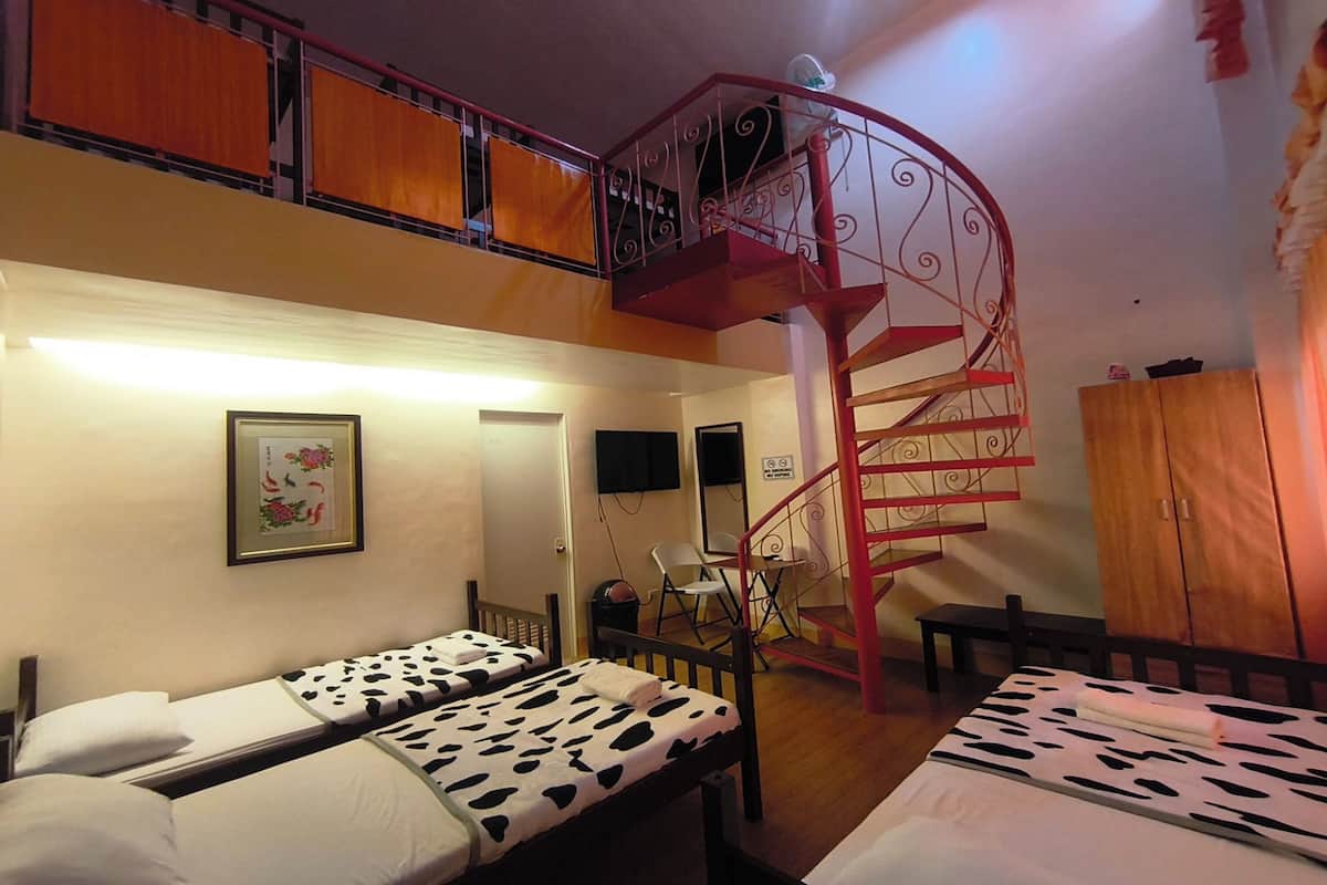 A dormitory room with two beds, a red spiral staircase, a wooden wardrobe, and a framed picture on the wall.