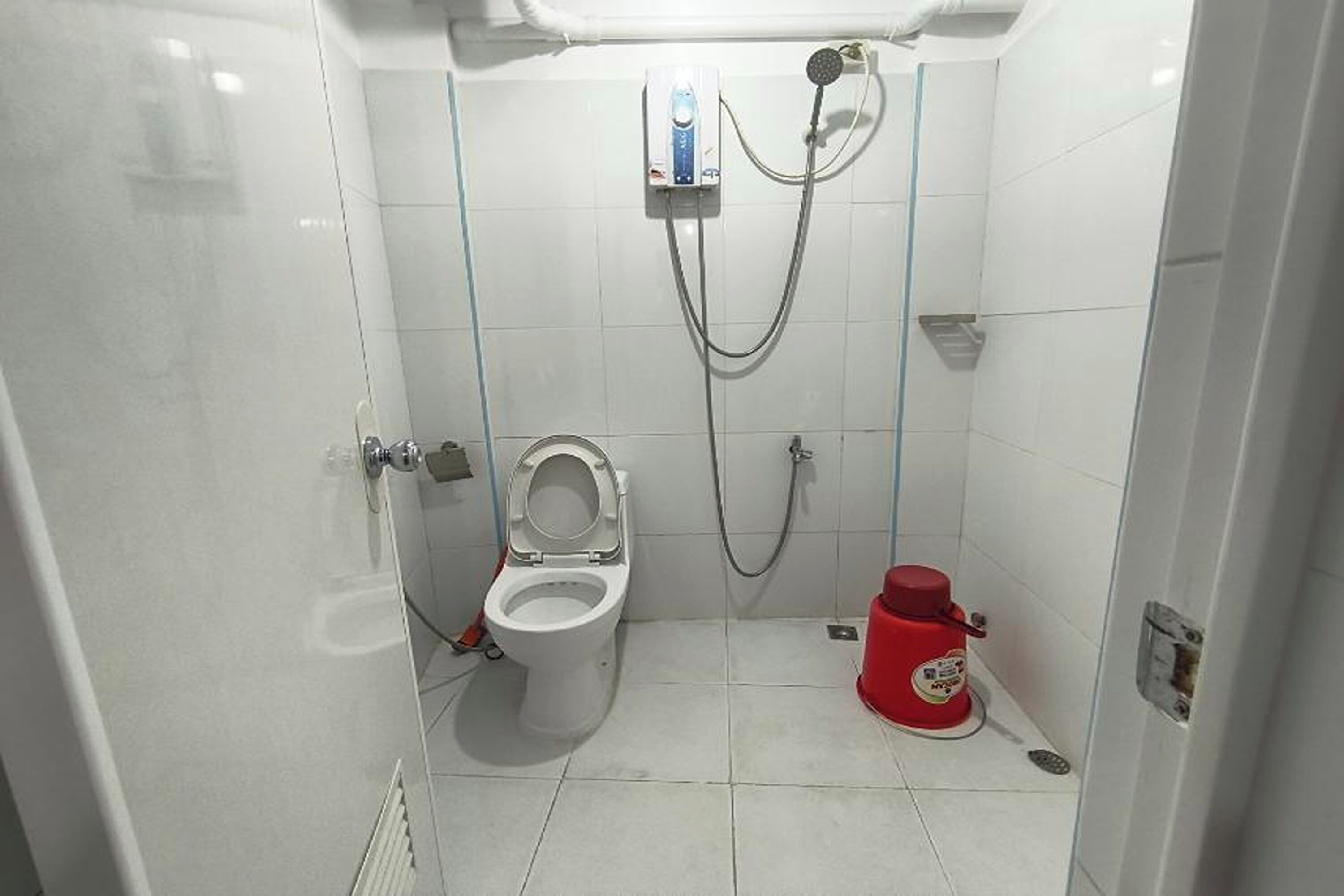 Un baño pequeño y funcional con inodoro, ducha y un extintor rojo.