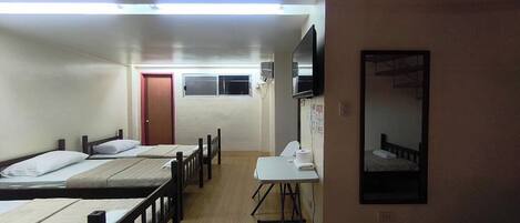 Un dormitorio con cuatro camas individuales, una mesita pequeña, un espejo y una puerta al fondo.