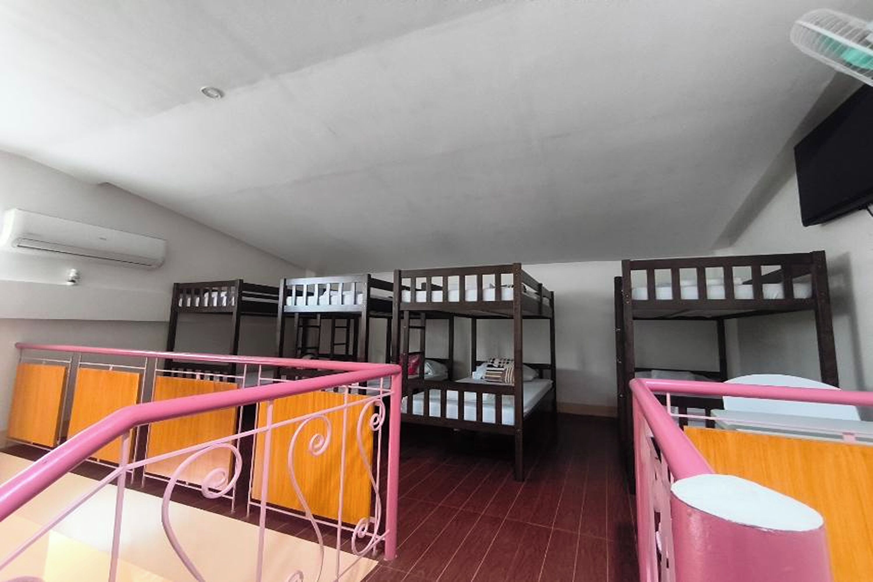 A dormitory room with bunk beds, a pink railing, and a ceiling fan.