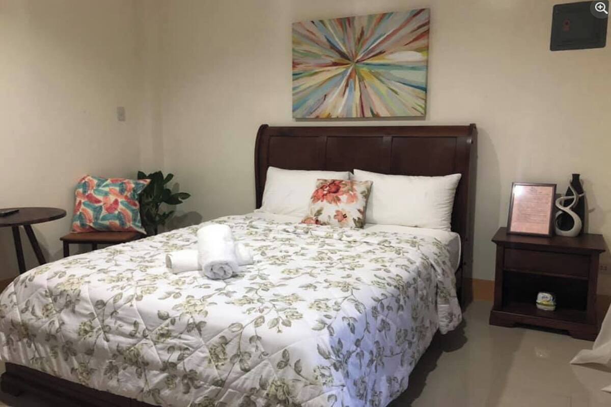 A neatly made bed with floral bedding, a bedside table with a lamp, and a wall-mounted artwork.