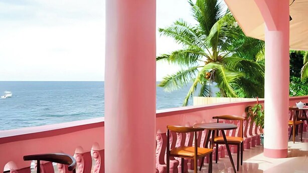 Uma área de estar coberta ao ar livre, com colunas e cadeiras cor-de-rosa, com vista para o mar.