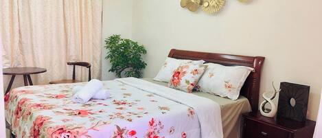 A neatly made bed with floral bedding, a bedside table with a vase, and a wall decoration.