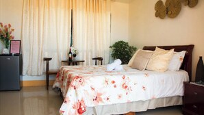 Quarto de hotel com cama, escrivaninha, cadeira, planta e decoração na parede.