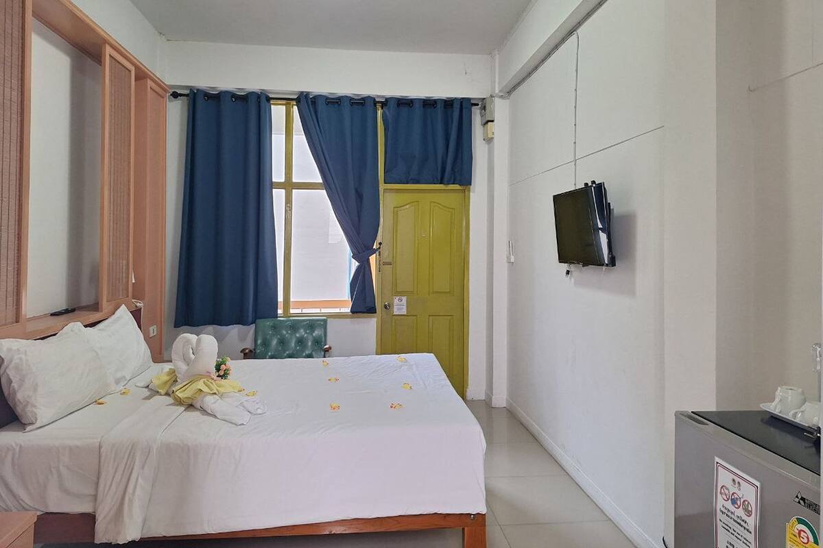 Een hotelkamer met een bed, een aan de muur bevestigde televisie, een bureau met een computer en een raam met gordijnen.