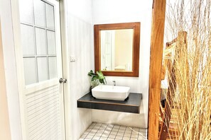 A bathroom with a white sink, a wooden-framed mirror, and a potted plant. - Bann Kam B&B (Krabi)