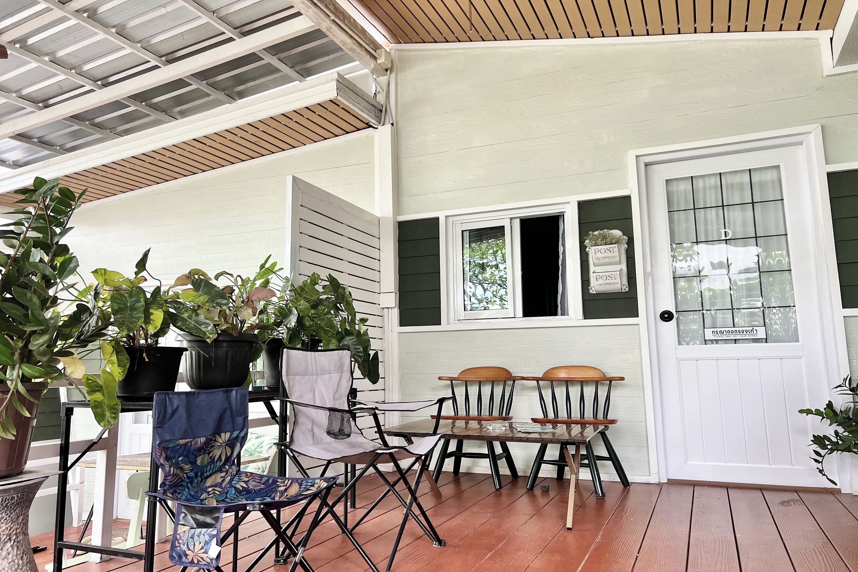 A covered porch with a wooden table and chairs, potted plants, and a door with a sign.