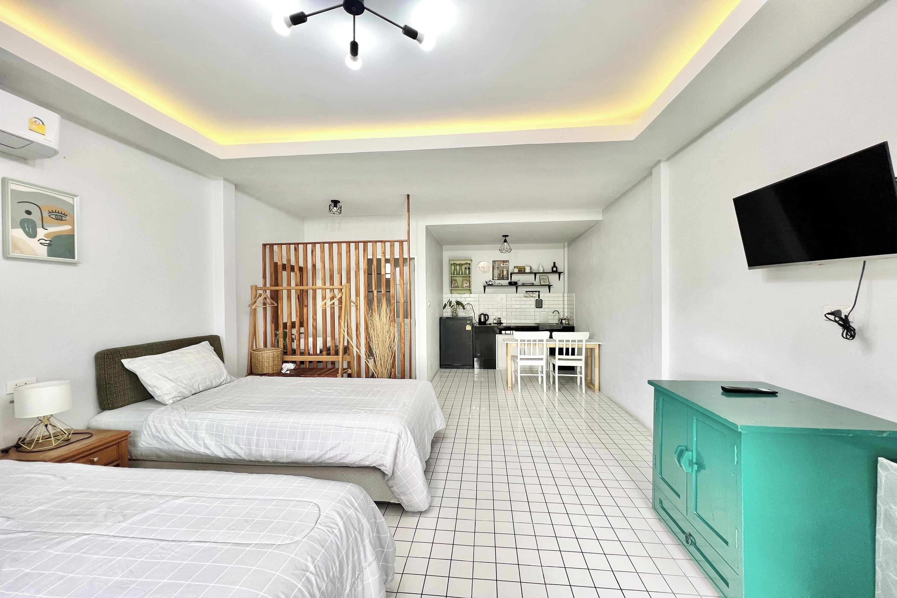 A modern hotel room with two beds, a kitchenette, a TV, and a teal dresser.
