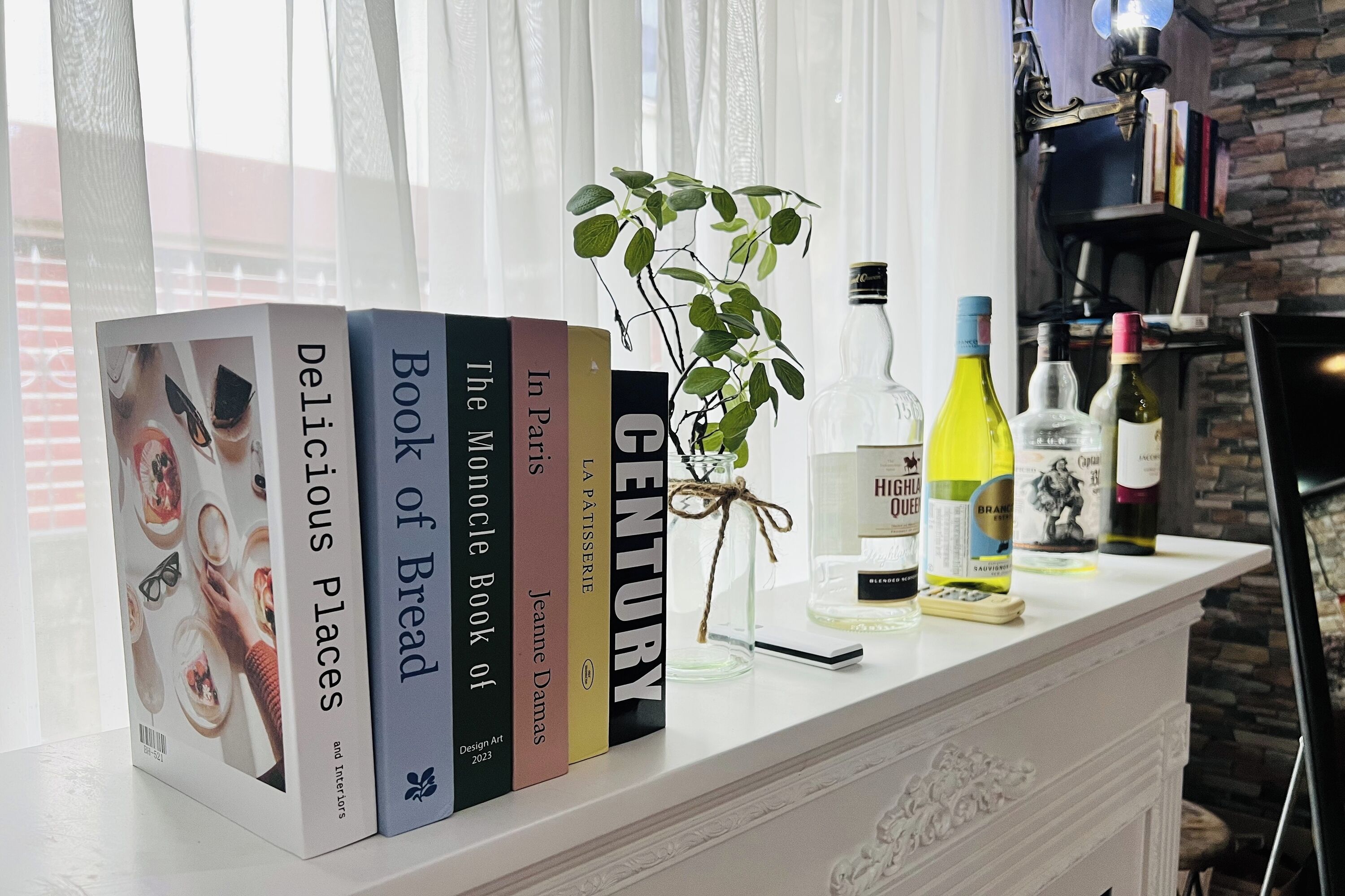 A bookshelf with books and decorative items, a plant, and bottles on a white shelf.