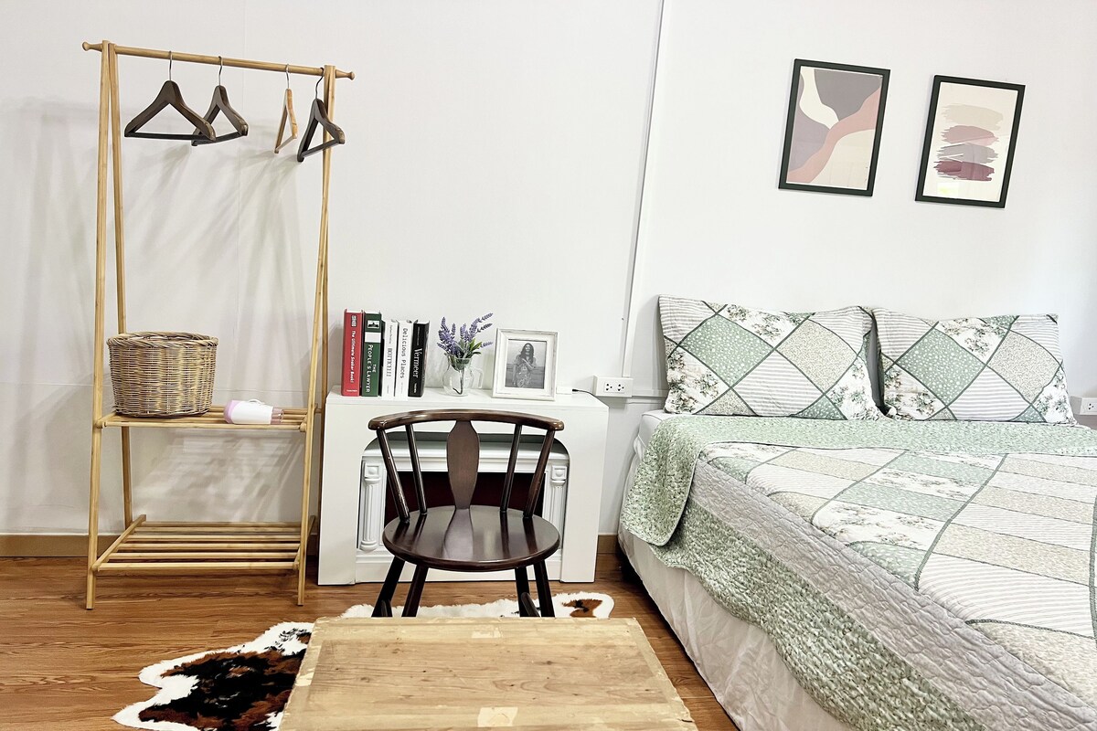 A bedroom with a bed, a chair, a small table, a hanging clothes rack, and a rug.