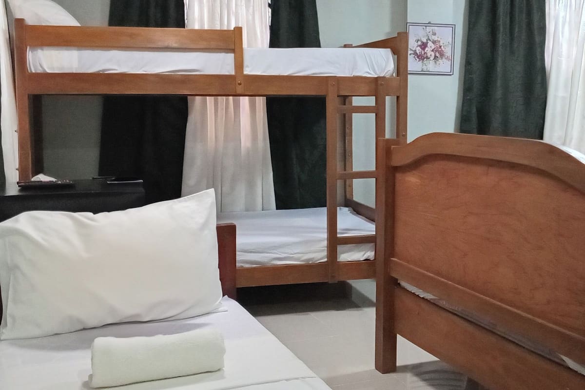 Habitación con literas, cabecera de madera, ropa de cama blanca y una mesita con un control remoto.