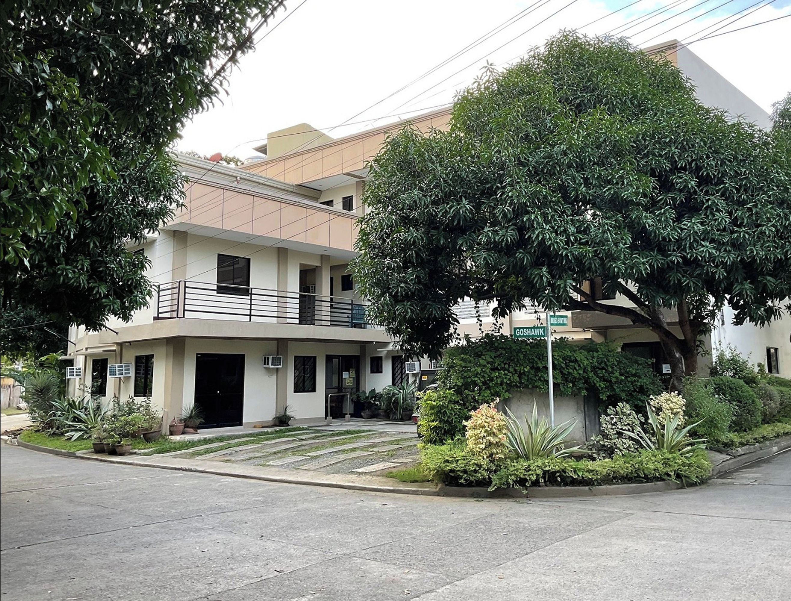 A multi-story building with a balcony, surrounded by lush greenery and a well-maintained garden.