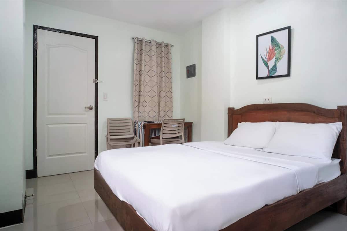 Una cama bien hecha con sábanas blancas, un cabecero de madera, una mesita con sillas y un cuadro en la pared.