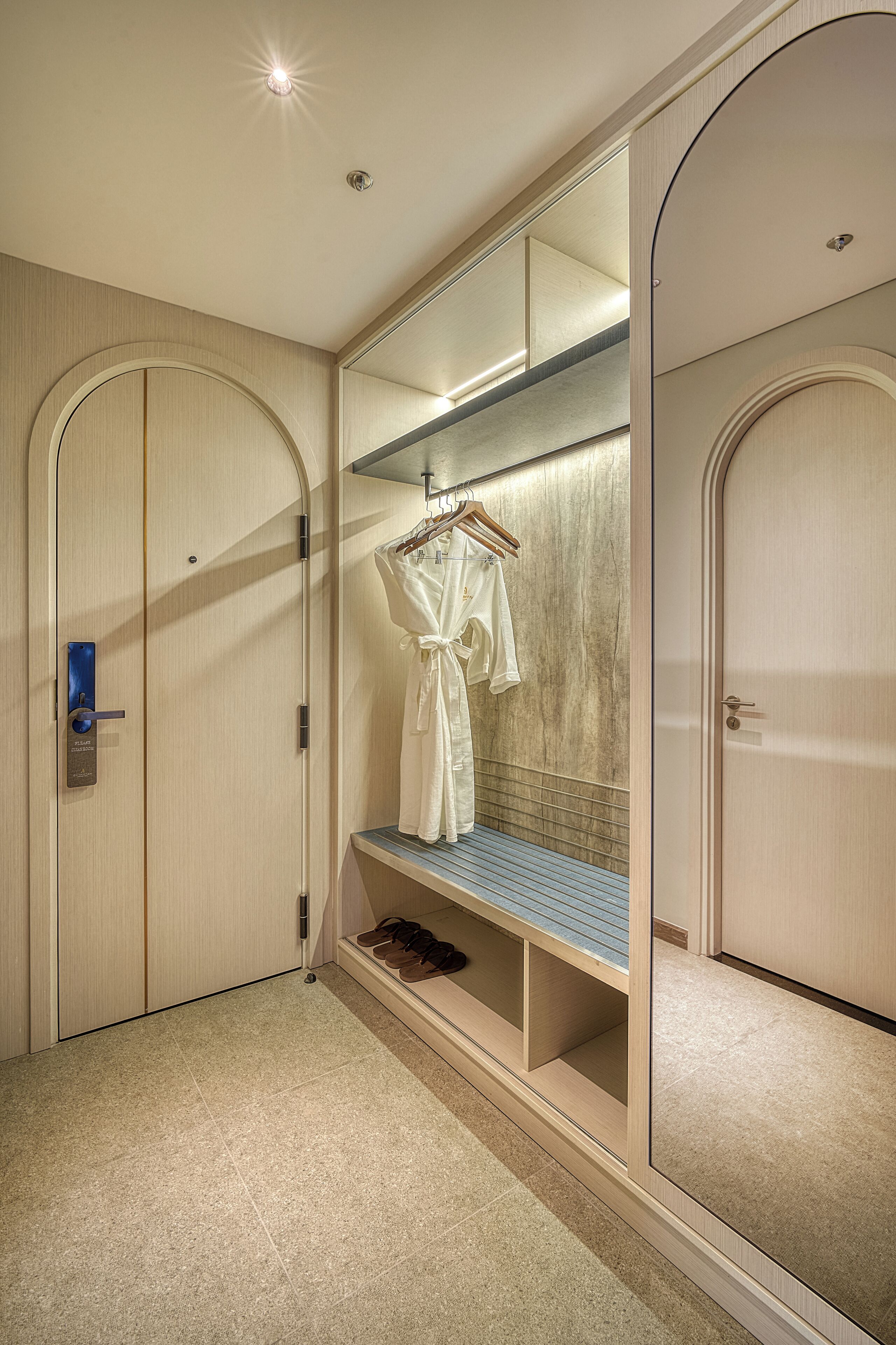 Een hotelkamer met een grote spiegel, een badjas en een schoenenrek.