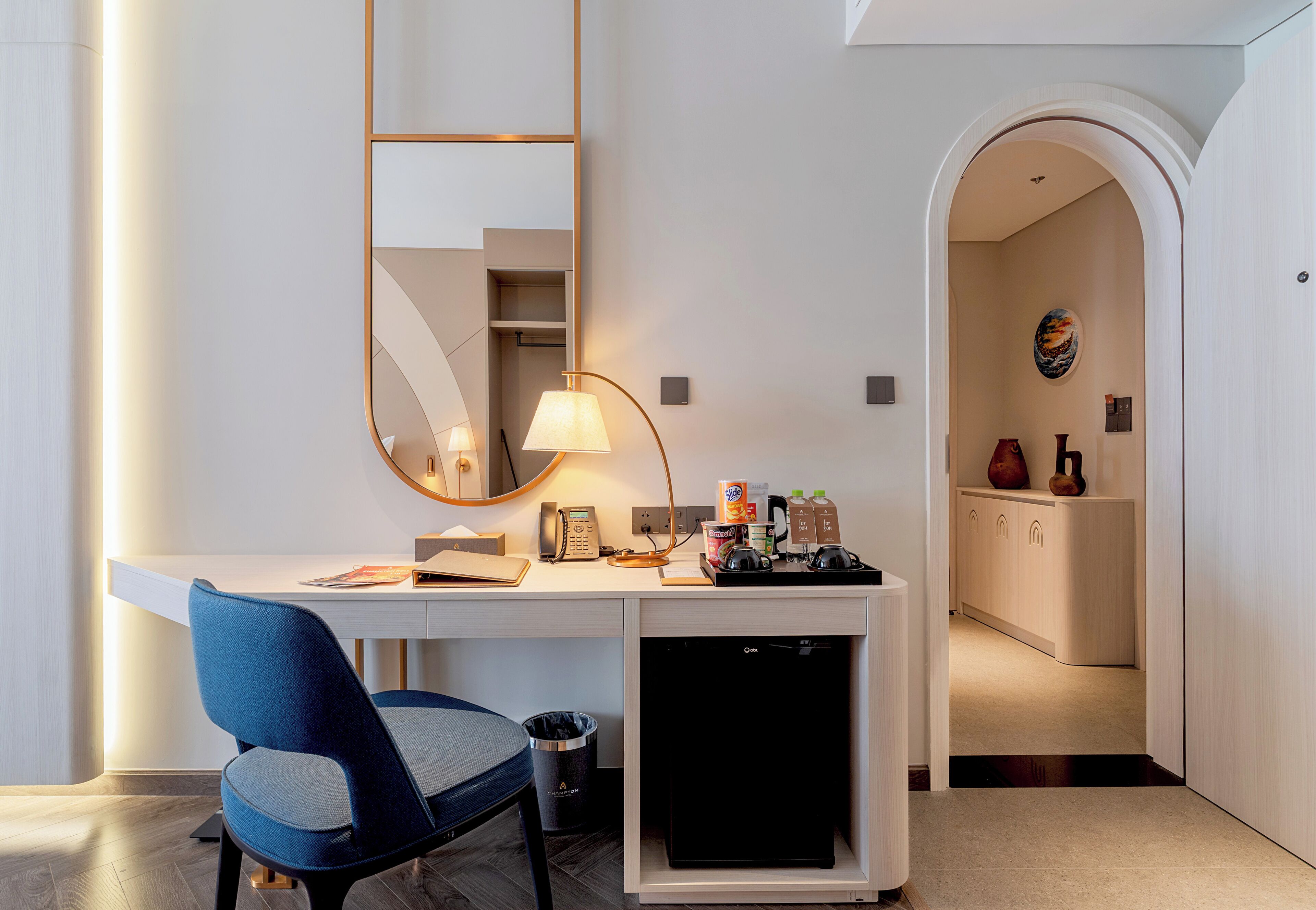 Ein modernes Hotelzimmer mit Schreibtisch, Stuhl, Lampe und einem kleinen Kühlschrank.