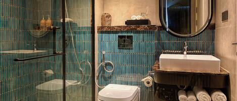 Un baño moderno con ducha de vidrio, inodoro blanco, lavamanos con encimera de mármol y un espejo grande.