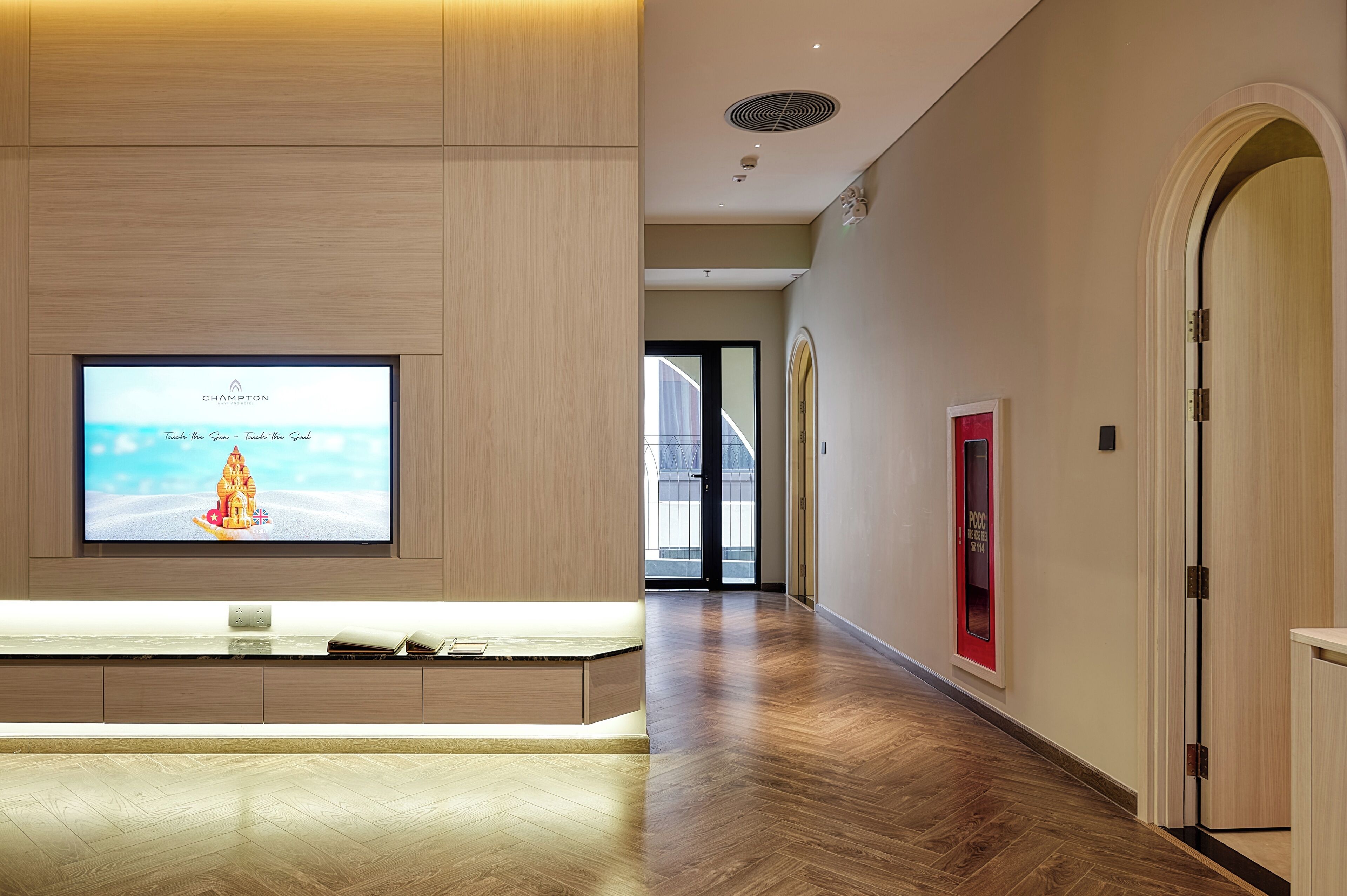Un hall d’hôtel moderne doté d’un grand téléviseur à écran plat affichant un message de bienvenue, d’un comptoir d’accueil en bois et d’un plancher en bois.