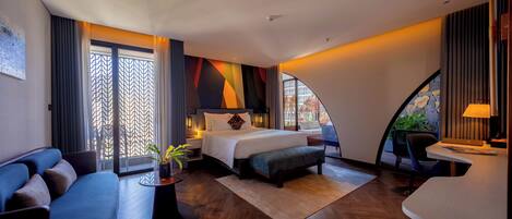 A modern hotel room with a bed, sofa, desk, and a view of the outdoors.