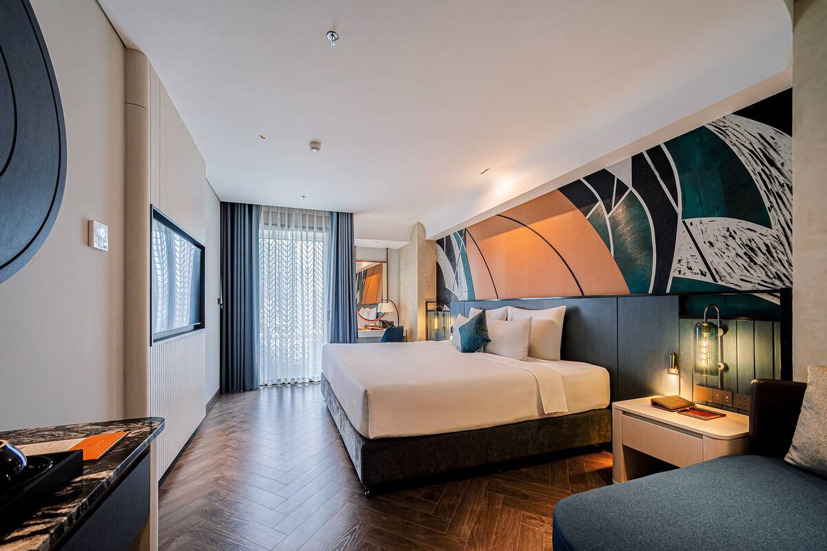 A modern hotel room with a large bed, a desk, a chair, and a TV.