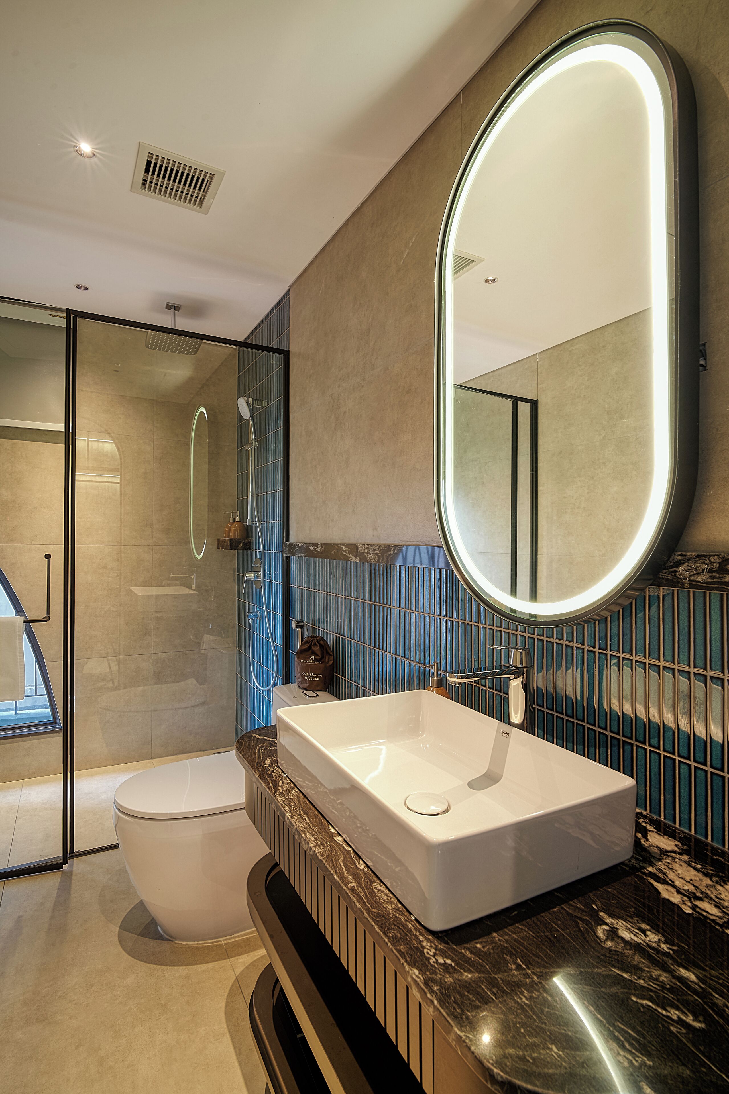 Un baño moderno con un espejo grande, un lavamanos blanco y una ducha con mampara de vidrio.