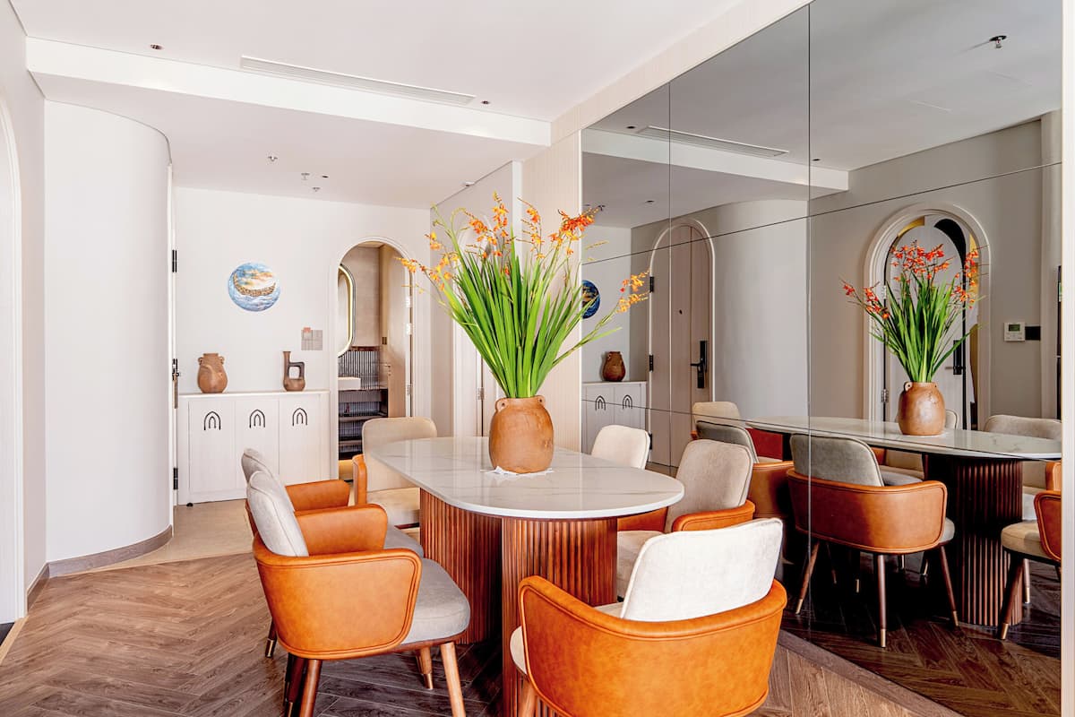 A modern dining area with a round table, orange chairs, and a vase with flowers.