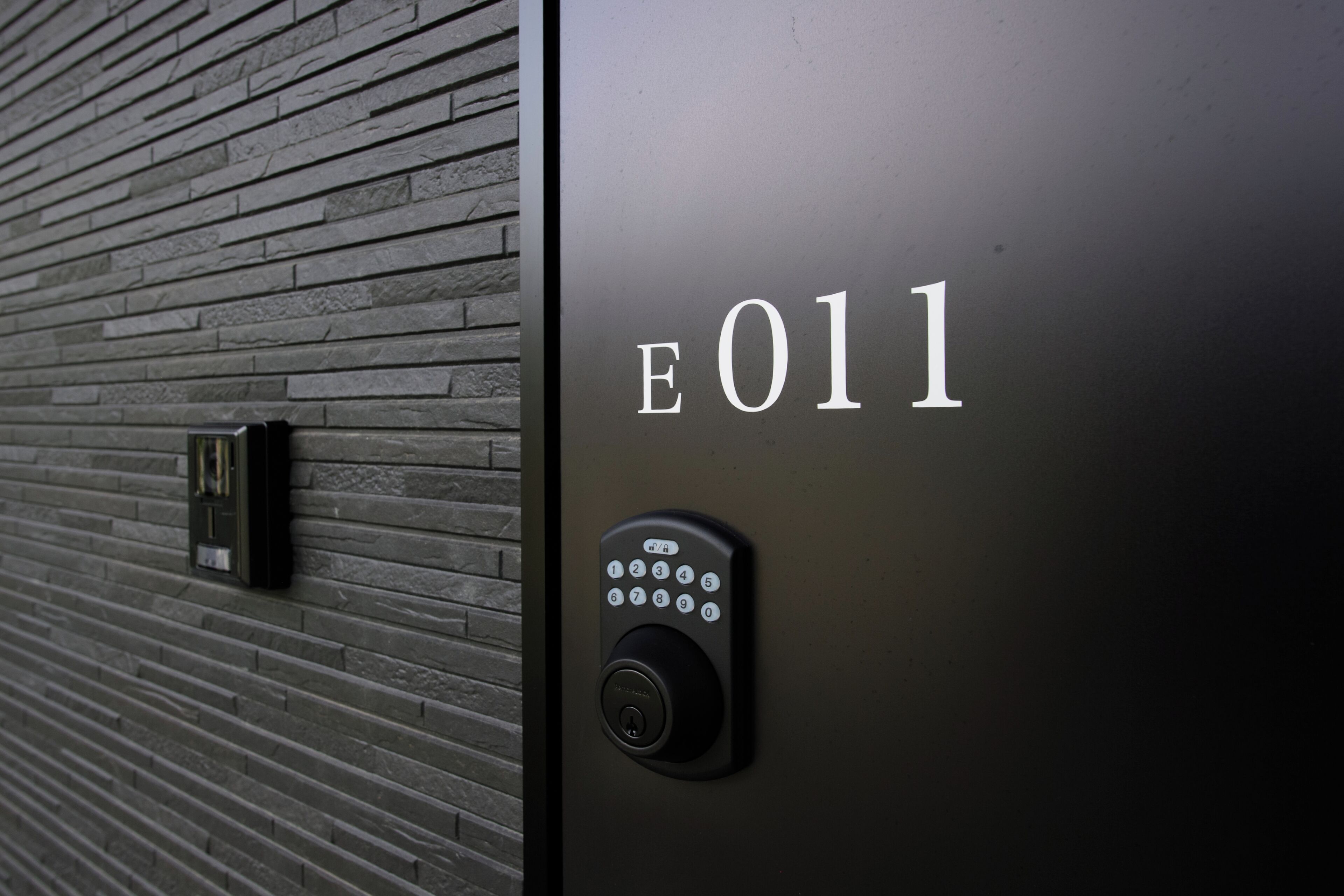 A modern door with a keypad and the number 'E011' indicating the room number.