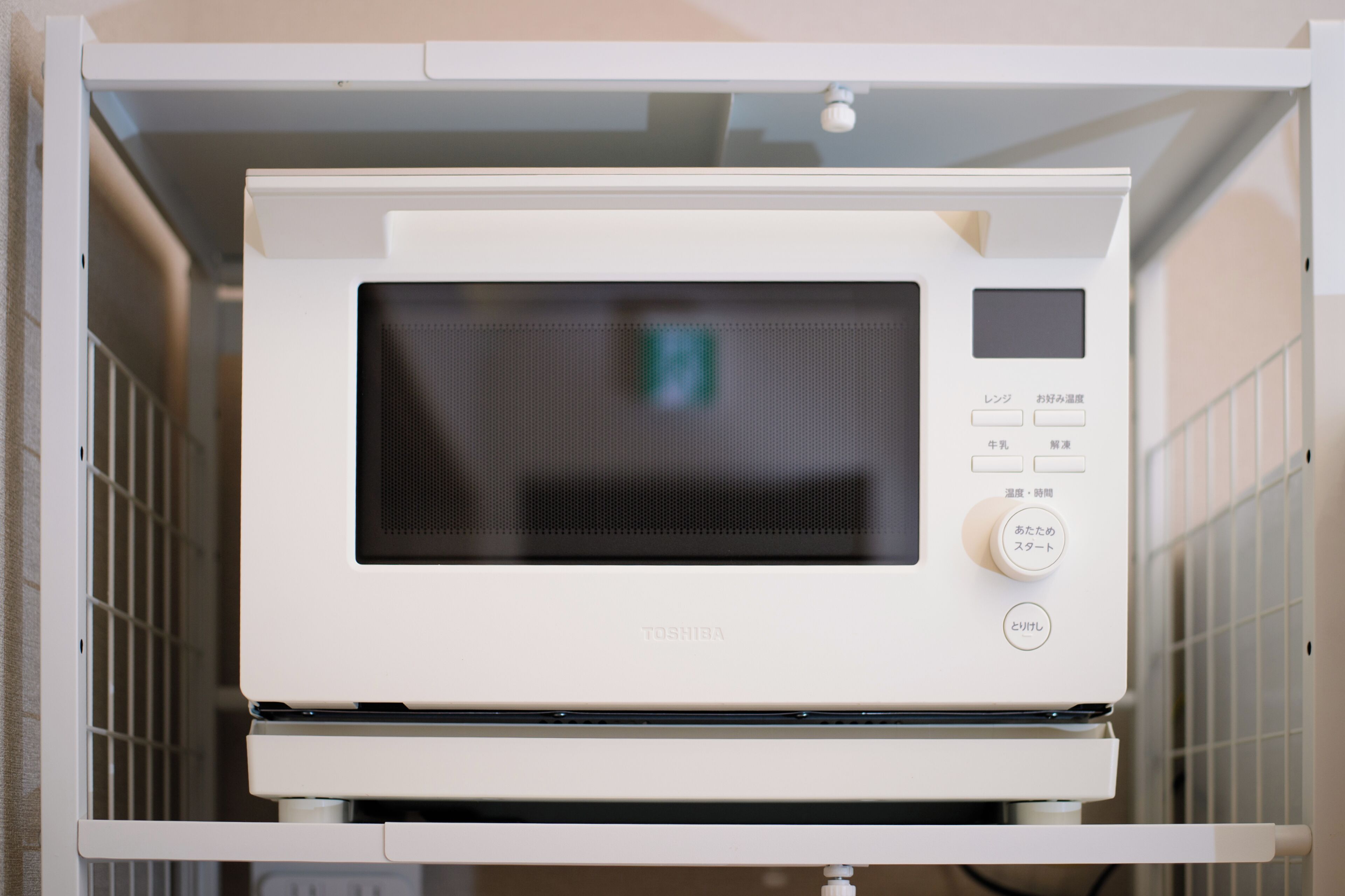 A white microwave oven with a digital display and control panel, mounted on a white cabinet.
