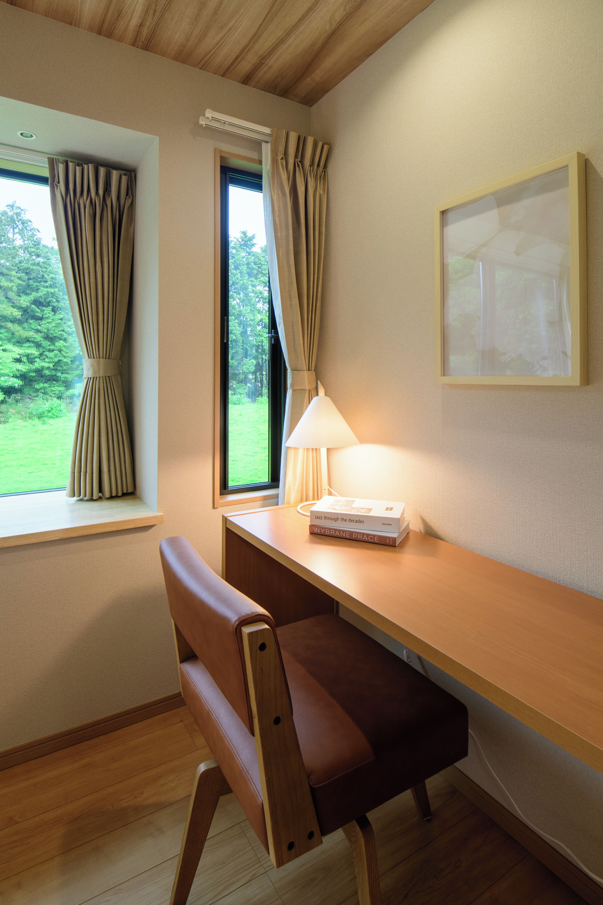 A room with a wooden desk, a chair, a lamp, and a window with curtains.