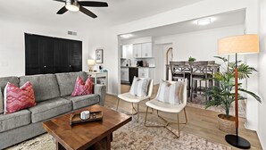 A modern living room with a grey sofa, two armchairs, a coffee table, a ceiling fan, and a dining area with a table and chairs. - Charming 1BR Getaway with King Bed in Royal Oak (Royal Oak)