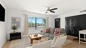 A modern living room with a grey sofa, white armchairs, a wooden coffee table, and a TV mounted on the wall. - Charming 1BR Getaway with King Bed in Royal Oak (Royal Oak)