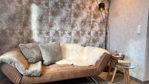A modern living room with a brown sofa, fluffy cushions, a glass coffee table, and a textured wall. - Studio apartment "Cozy" with terrace & parking space (Blankenburg)