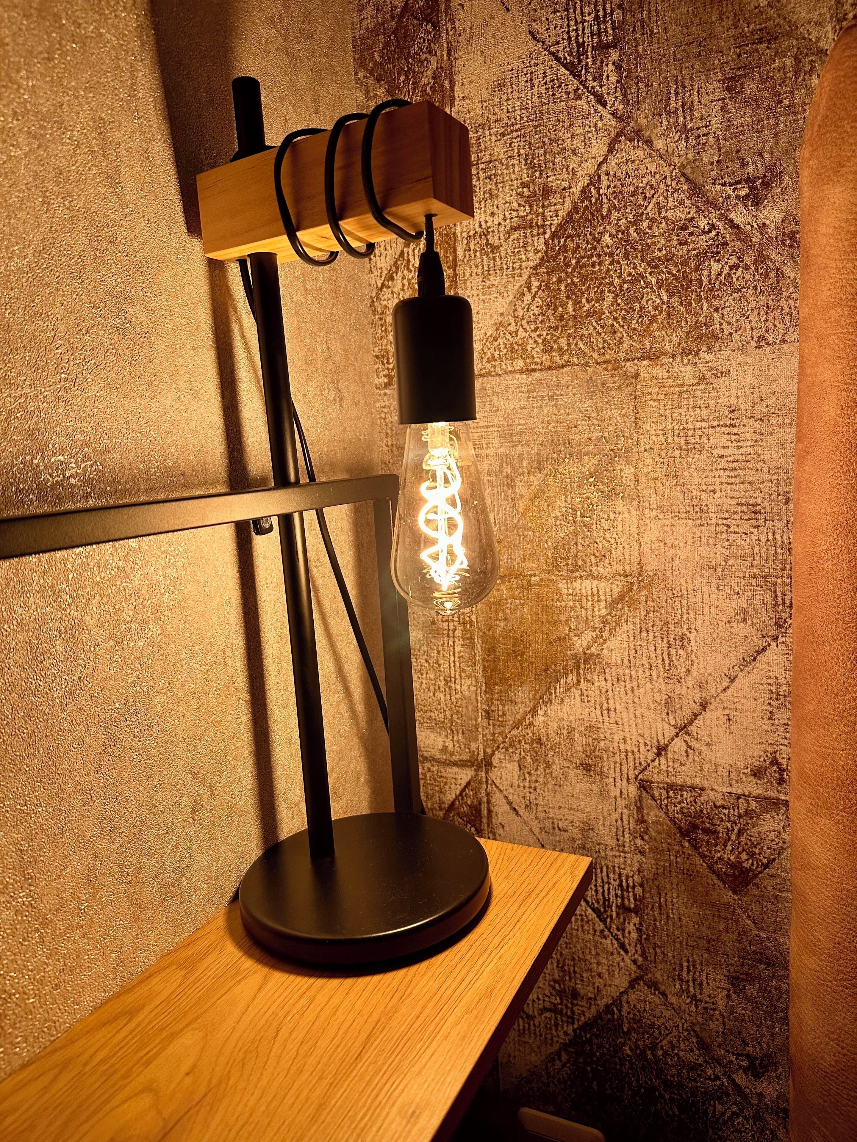 Eine Tischlampe mit Holzfuß und Glaskolben, der eine spiralförmige Glühbirne enthält.