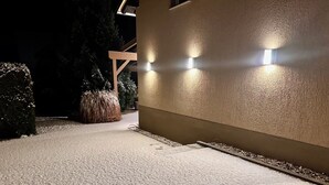 A pathway leading to a building with a textured wall and three wall-mounted lights. - Studio apartment "Cozy" with terrace & parking space (Blankenburg)