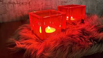 Two red square candle holders with lit candles on a fluffy red surface against a textured wall.