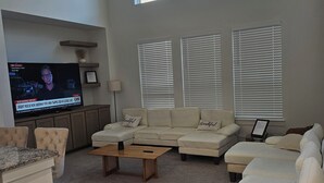 A living room with a TV, beige sofas, a coffee table, and large windows. - Spacious 5-bedroom house with WiFi, AC in brilliant Mesquite (Mesquite)