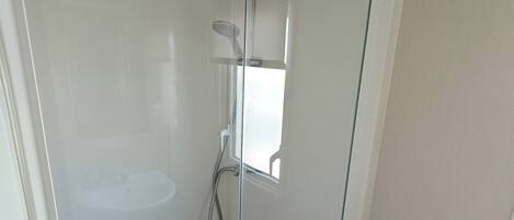 A glass-enclosed shower with a handheld showerhead and a built-in seat.