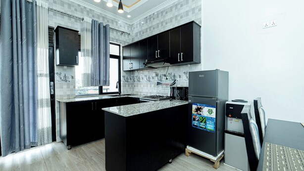 A modern kitchen with black cabinets, a granite countertop, a built-in oven, and a refrigerator with a digital display.