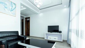 A modern living room with a black leather sofa, a white entertainment unit with a TV, and a glass coffee table.