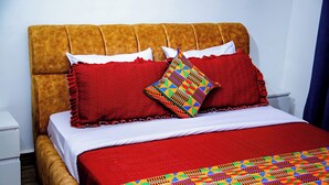Uma cama com um edredom vermelho, duas almofadas e um cobertor colorido.
