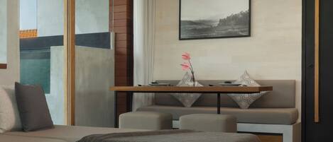 Un salon moderne avec un canapé, une table basse et une table à manger avec des chaises. Un tableau orne le mur et une fenêtre offre une vue agréable.
