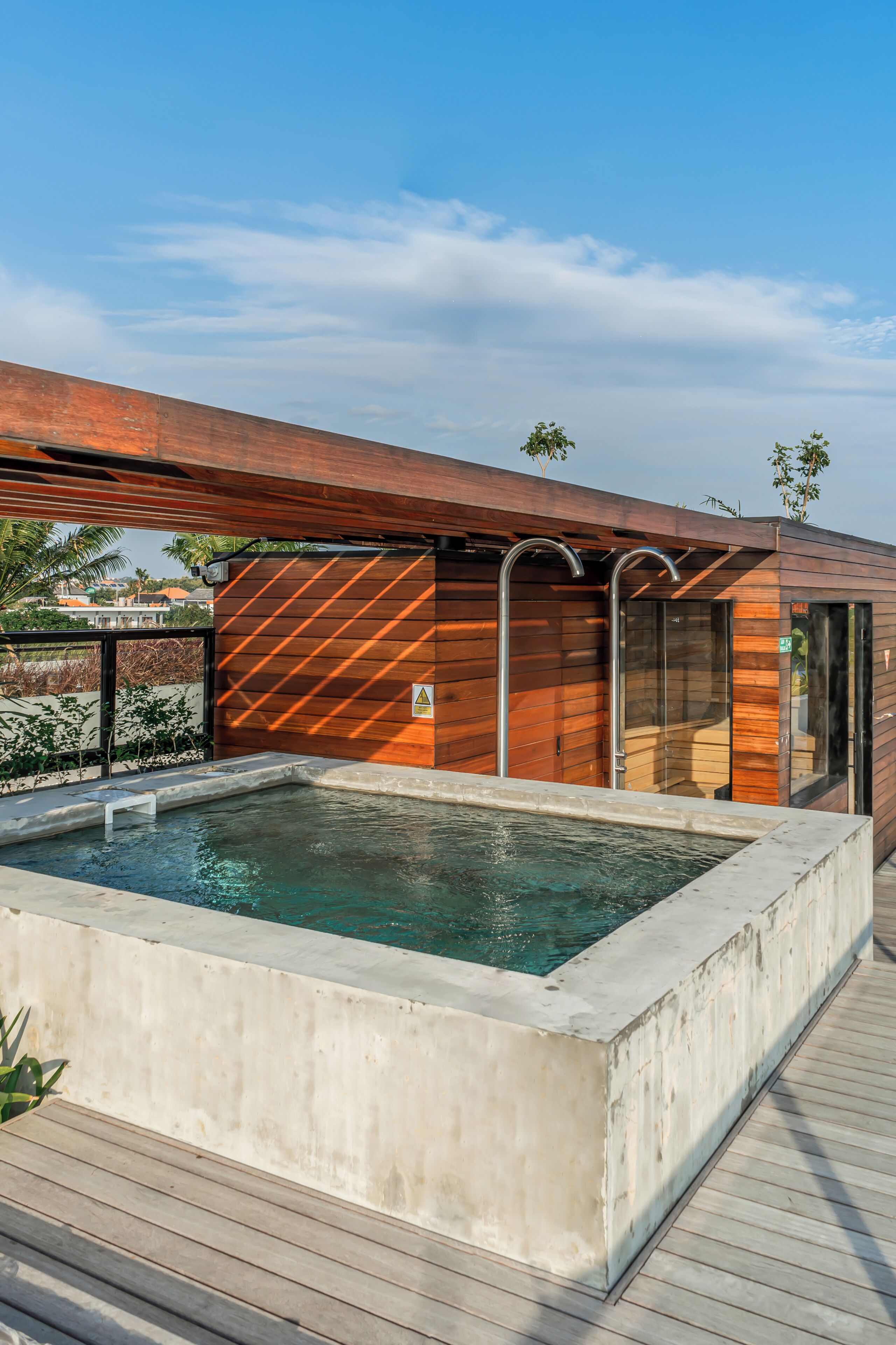 A modern outdoor pool area with a wooden deck, a concrete pool, and a metal roof structure.