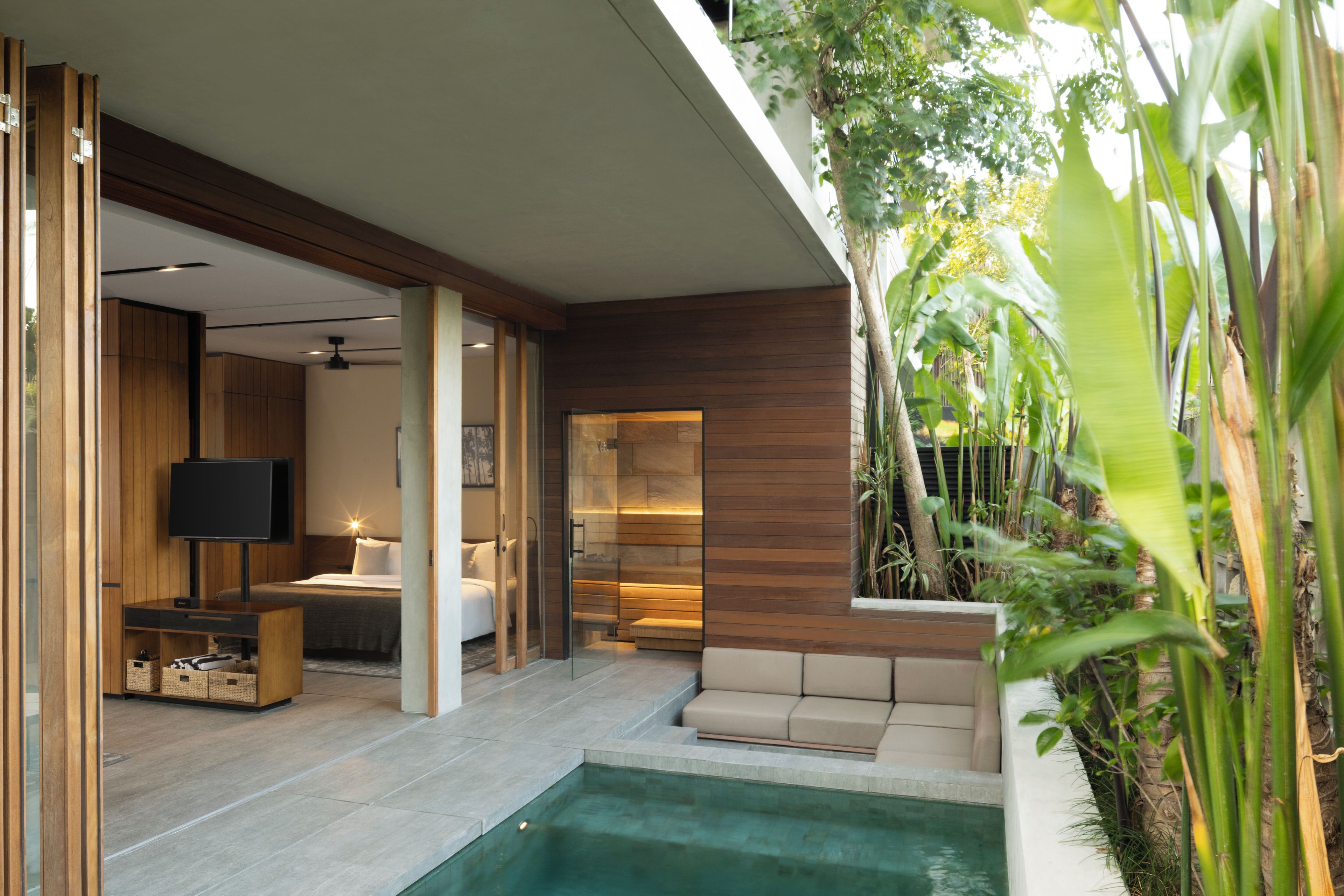 Una habitación de hotel moderna con puerta de cristal que da a un balcón, una piscina y una zona de estar con cojines.