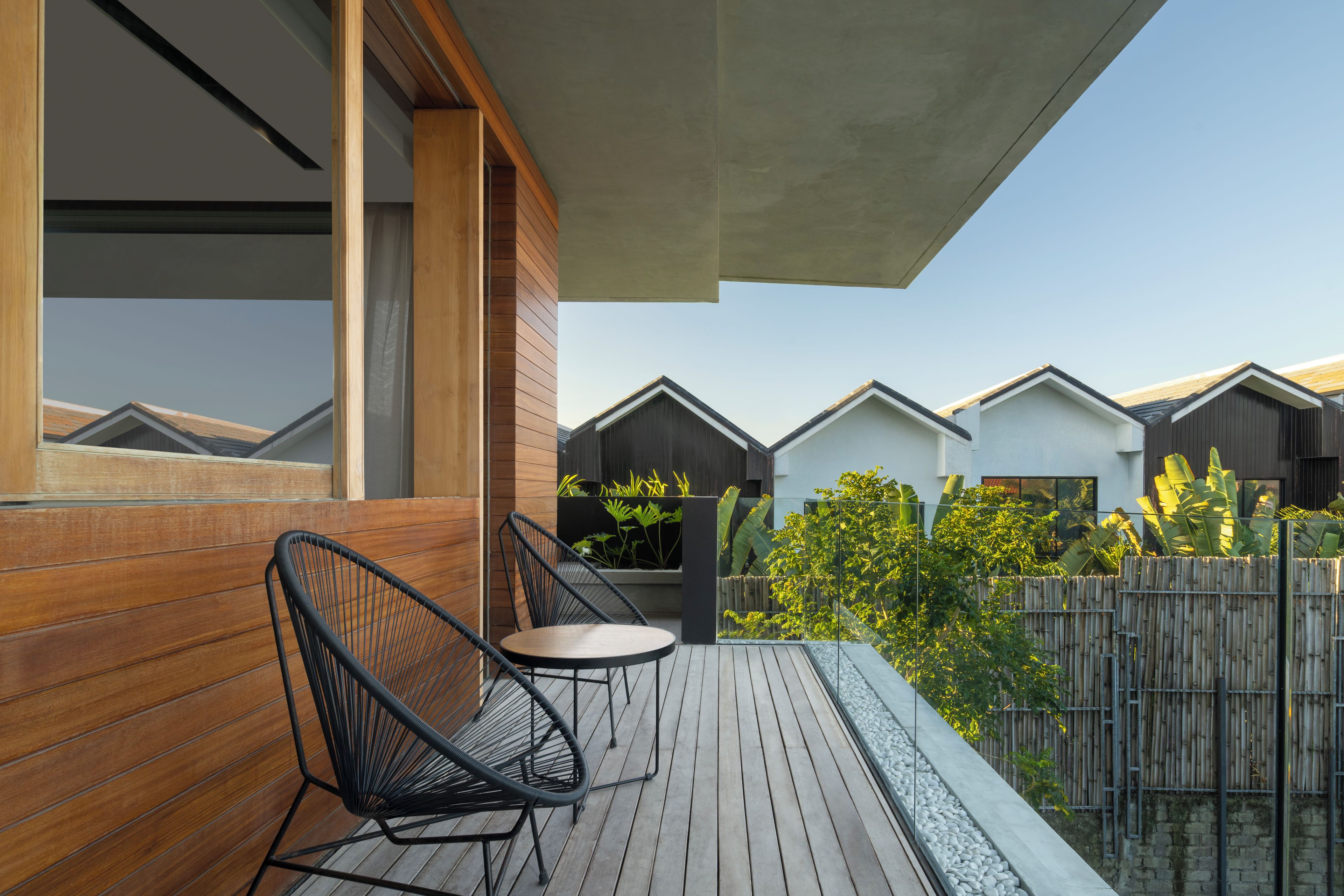 Une terrasse en bois avec une chaise et une petite table, entourée d’une clôture en bambou et de verdure.