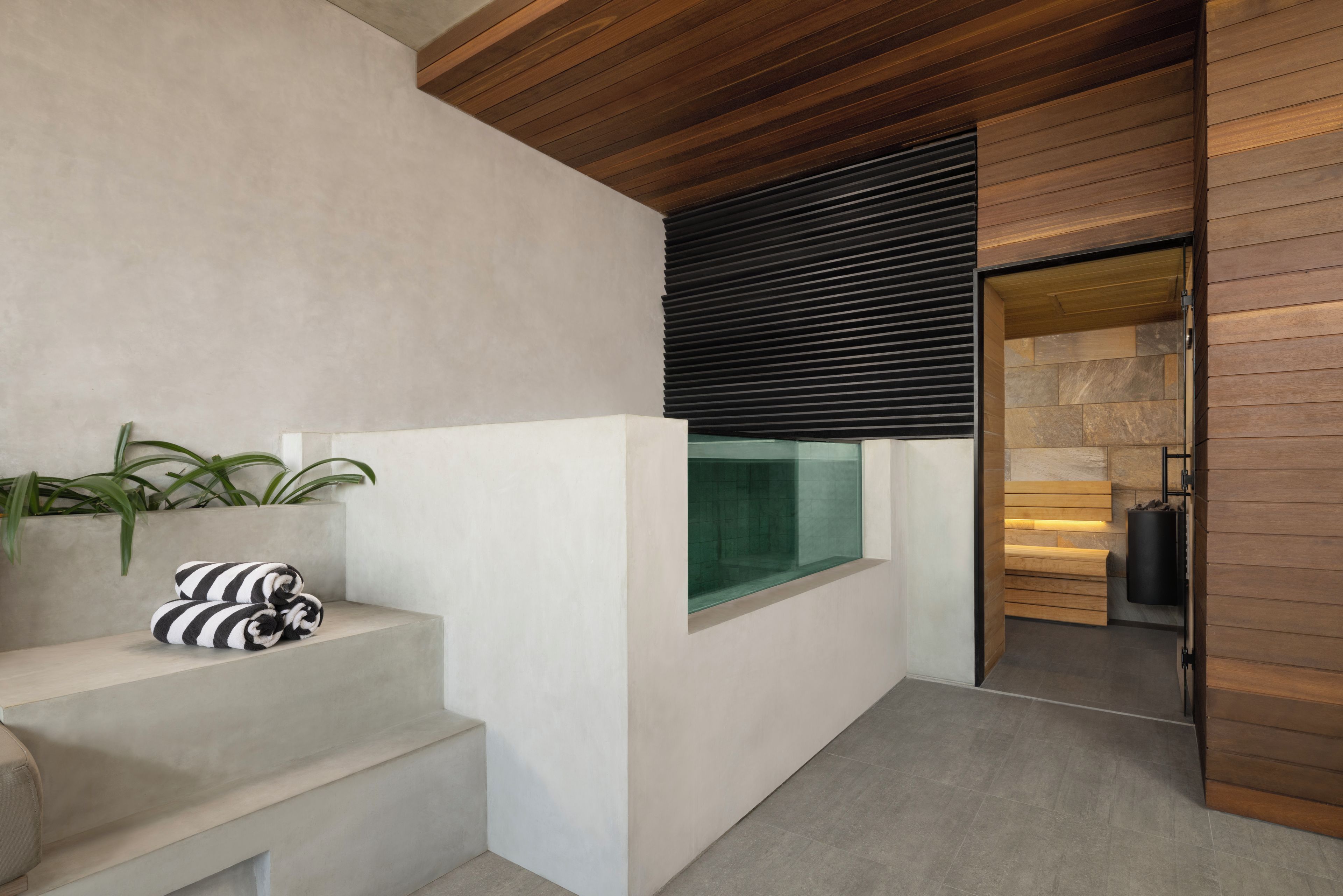 A modern interior with a staircase, a bench with pillows, a window with blinds, and a fireplace.