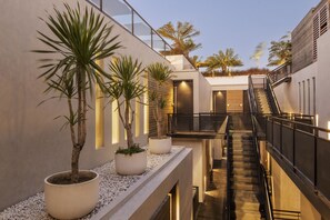 A modern building with a central staircase, potted plants, and a balcony overlooking a garden. - Body Factory Lifestyle Residence Canggu (Canggu)